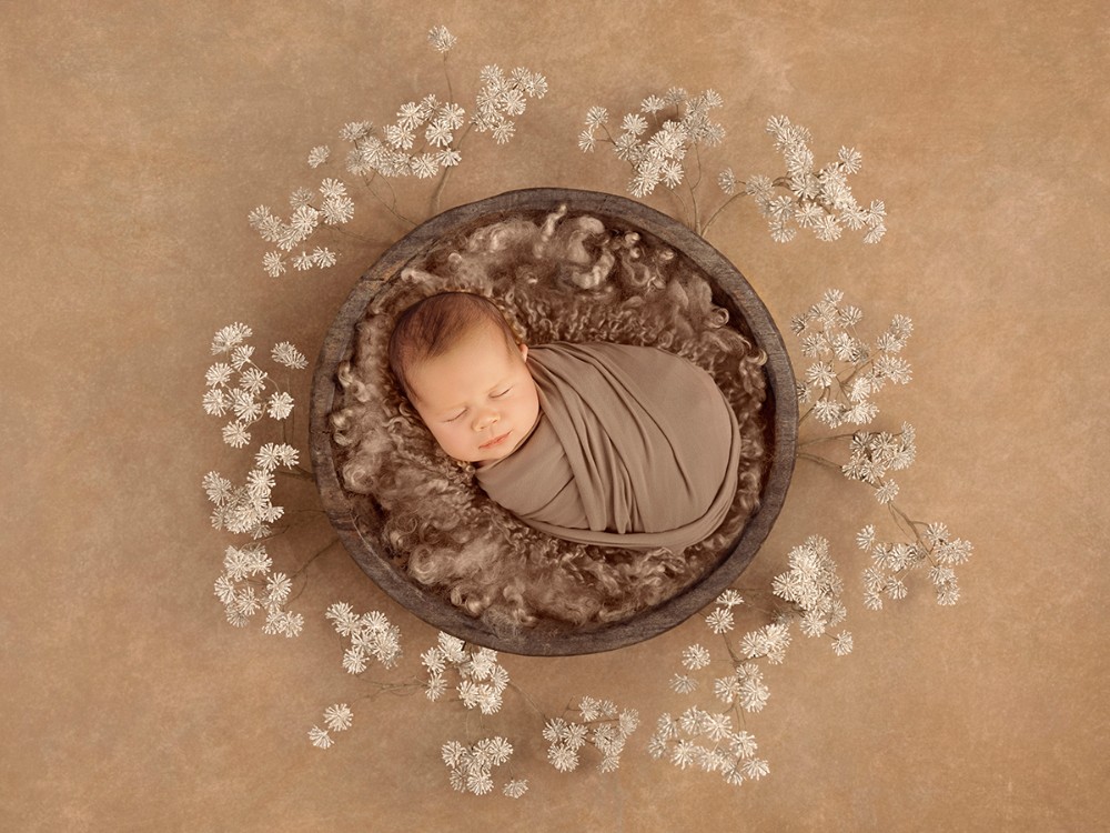 Artistic newborn portrait of a sleeping baby wrapped in neutral tones and surrounded by delicate flowers, created by a fine art newborn photographer near Maldon, Essex.