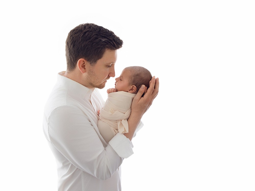 Father gently holding his newborn baby in a timeless light-filled portrait, photographed during a bespoke newborn photography session near Danbury, Essex.