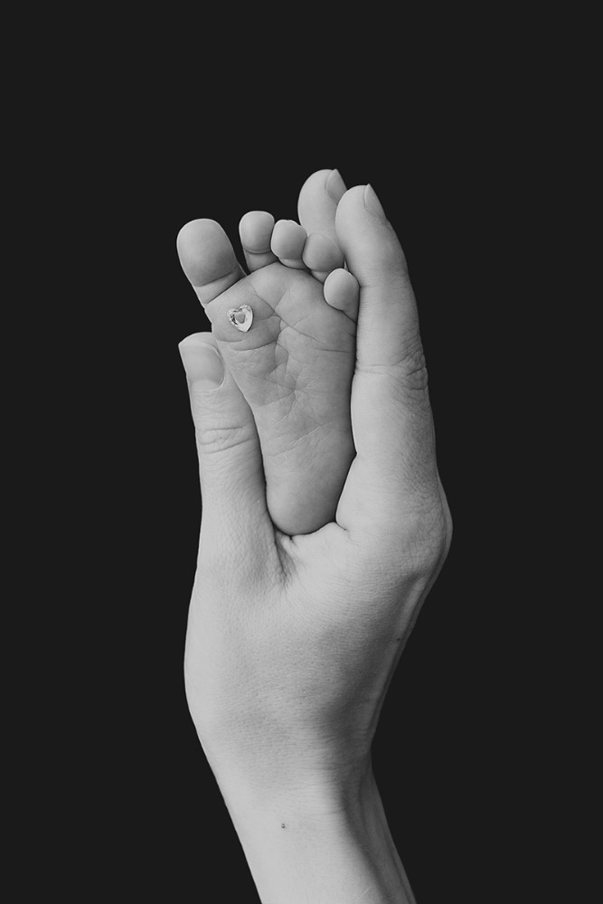 Black and white fine art newborn photograph of a tiny baby foot held gently in a parent's hands, photographed by an Essex newborn photographer near Chelmsford.