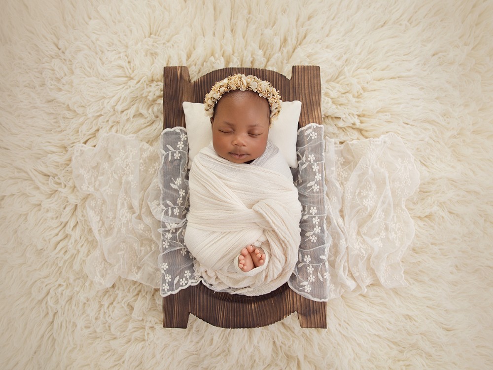 Sleeping newborn baby wrapped in soft ivory and styled with delicate lace and a floral headband for a fine art newborn photography session near Braintree, Essex.
