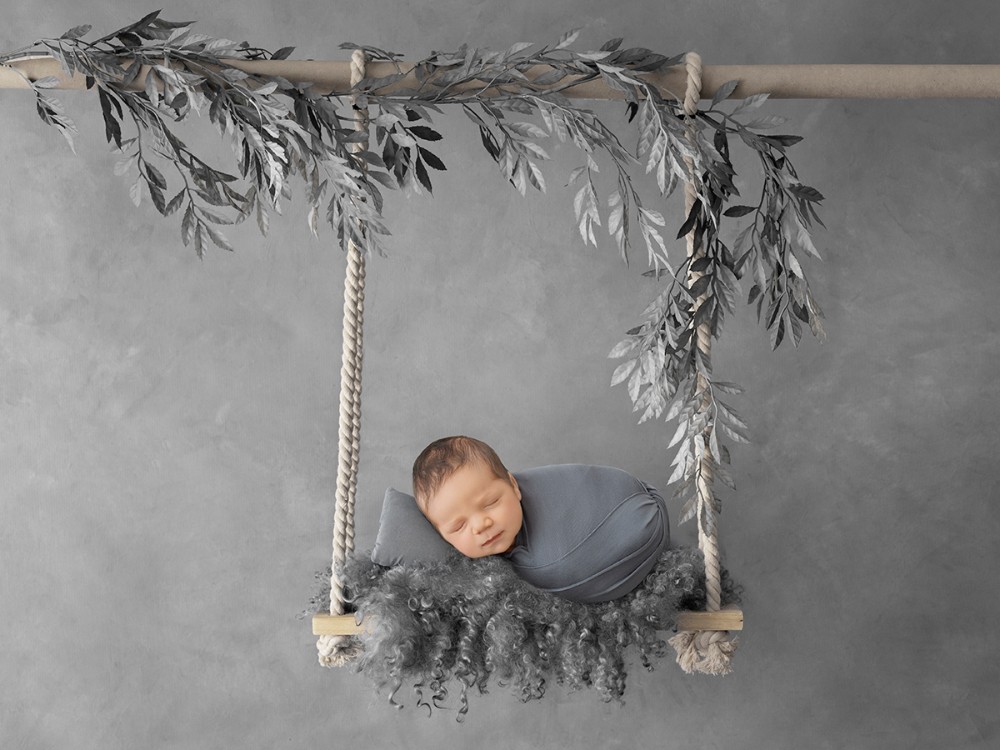 Fine art newborn portrait of a sleeping baby styled on a decorative swing in soft grey tones during a bespoke newborn photography session near Braintree, Essex.