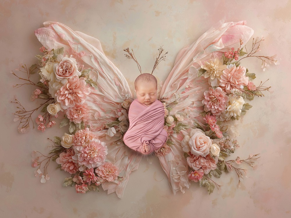 Sleeping newborn baby wrapped in dusty pink and surrounded by an elaborate floral butterfly design, creating a bespoke fine art newborn portrait in Witham, Essex.