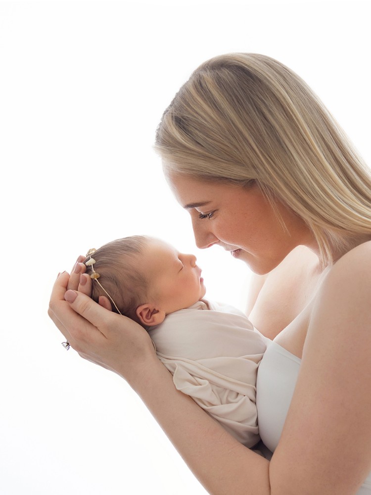 Mother lovingly holding her newborn baby close in a soft, timeless portrait created during an in-home newborn photography session near Kelvedon, Essex.