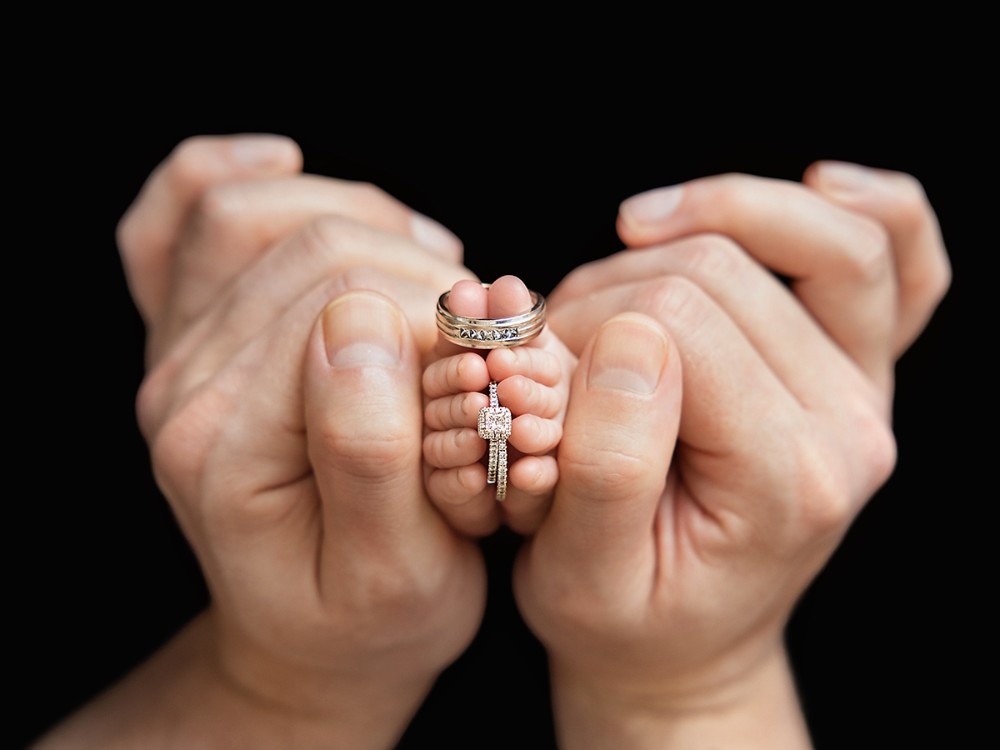 Tiny newborn feet held between parents' hands with their wedding rings, creating an emotional newborn detail portrait during a photography session near Maldon, Essex.