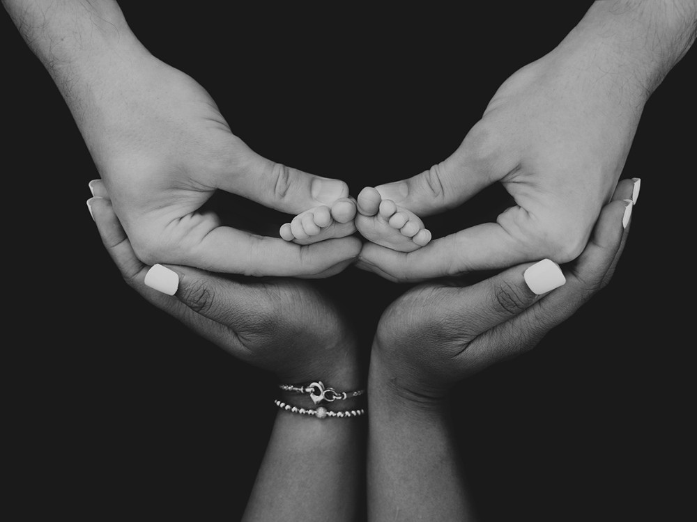 Black and white newborn detail portrait of tiny baby feet surrounded by parents' hands, preserving family connection during a newborn session near Maldon, Essex.