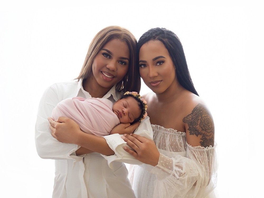 Two mothers lovingly holding their sleeping newborn baby in a refined family portrait during a professional newborn photography session near Colchester, Essex.