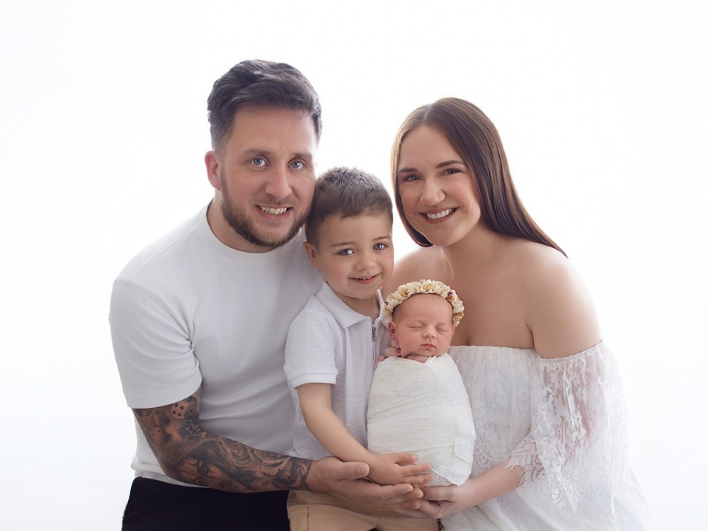 Parents and their young son holding their sleeping newborn baby in a timeless family portrait during an in-home newborn photography session near Chelmsford, Essex.