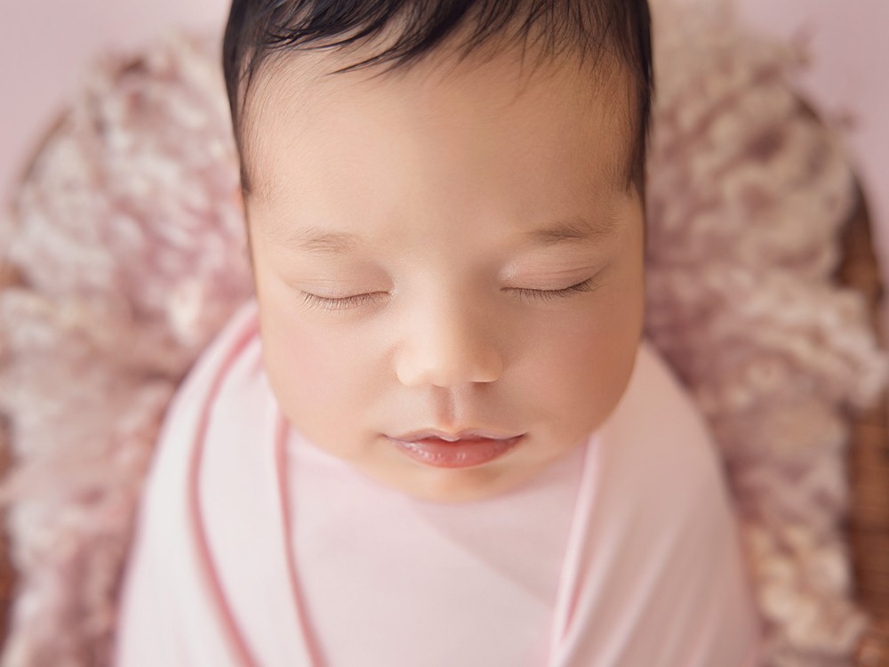 Close-up portrait of a peacefully sleeping newborn wrapped in soft pink, photographed during a bespoke newborn photography session in Witham, Essex.