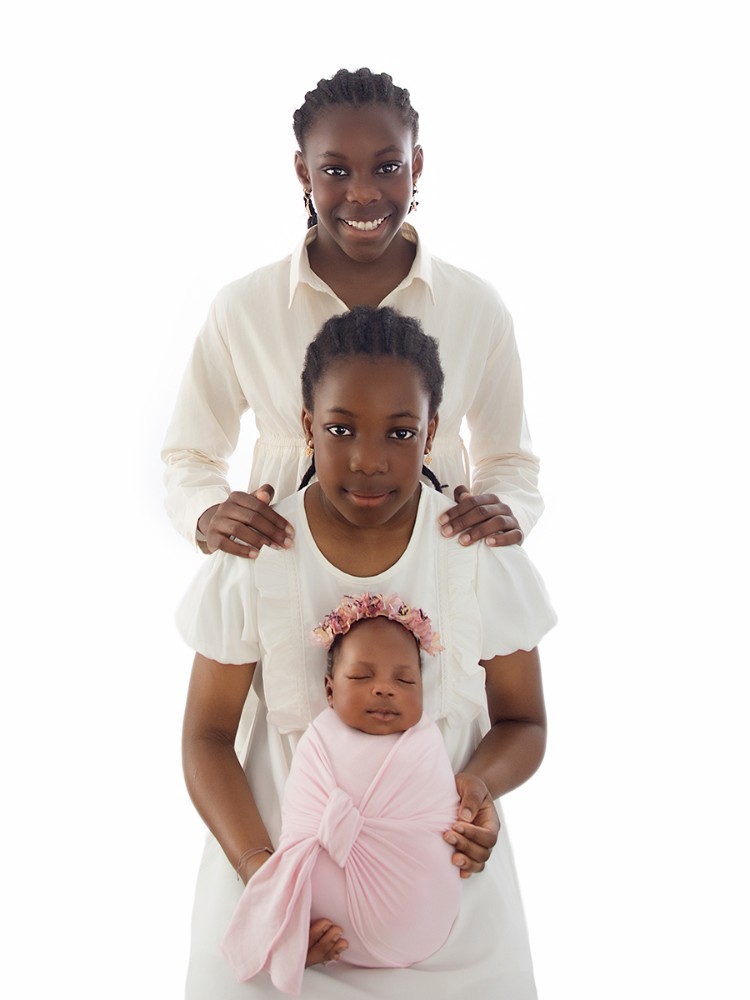 Newborn baby photographed with her two older sisters in a beautifully coordinated sibling portrait by an in-home newborn photographer serving Chelmsford, Essex.