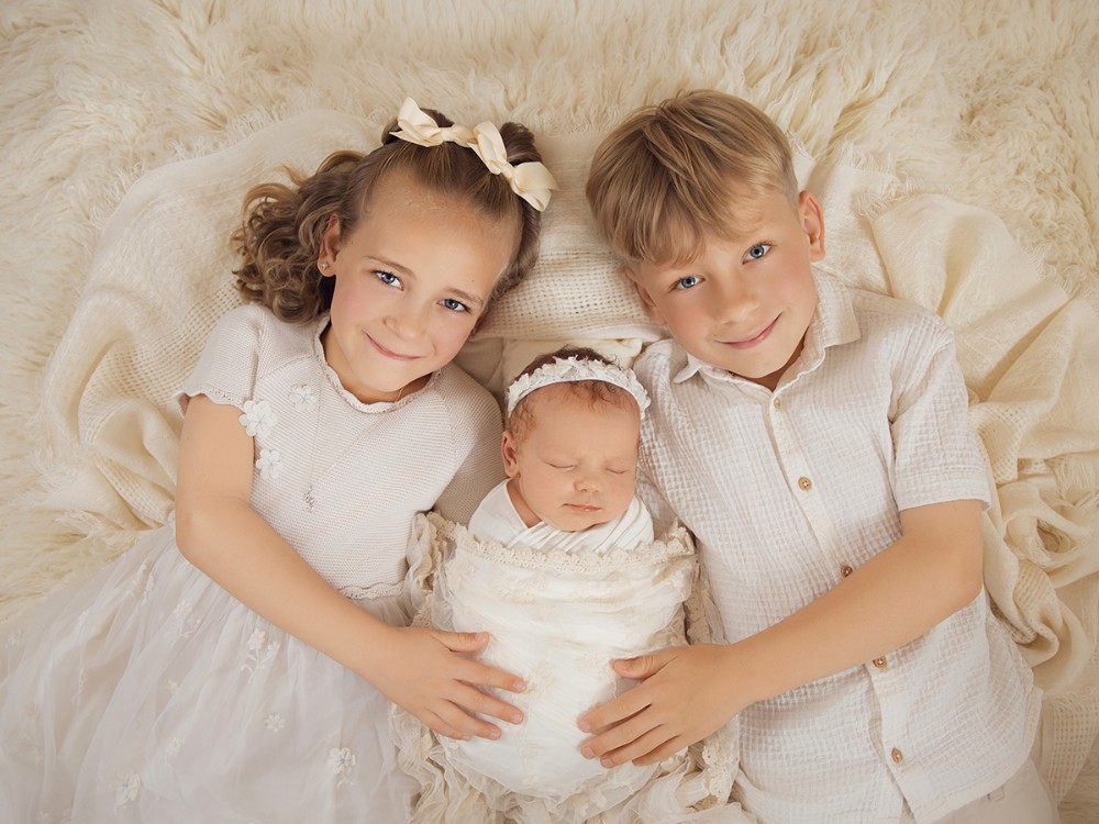 Newborn baby photographed with older brother and sister in a timeless neutral sibling portrait during an in-home newborn photography session near Colchester, Essex.