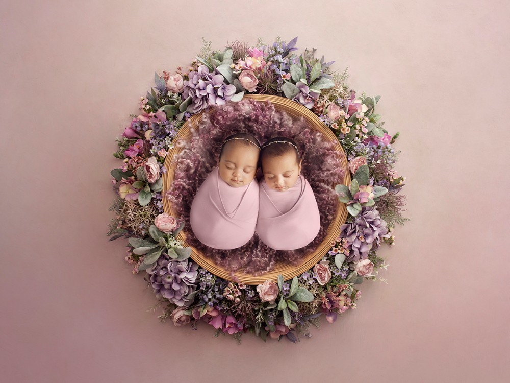 Fine art twin newborn photography featuring two sleeping babies surrounded by soft pink and purple florals, photographed near Braintree, Essex.