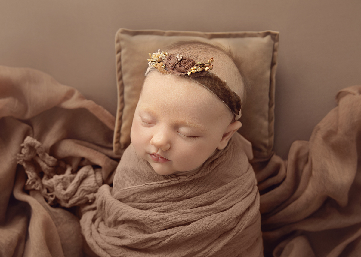 Peaceful sleeping newborn baby wrapped in soft brown fabric during a natural newborn photography session in Wickford Essex.