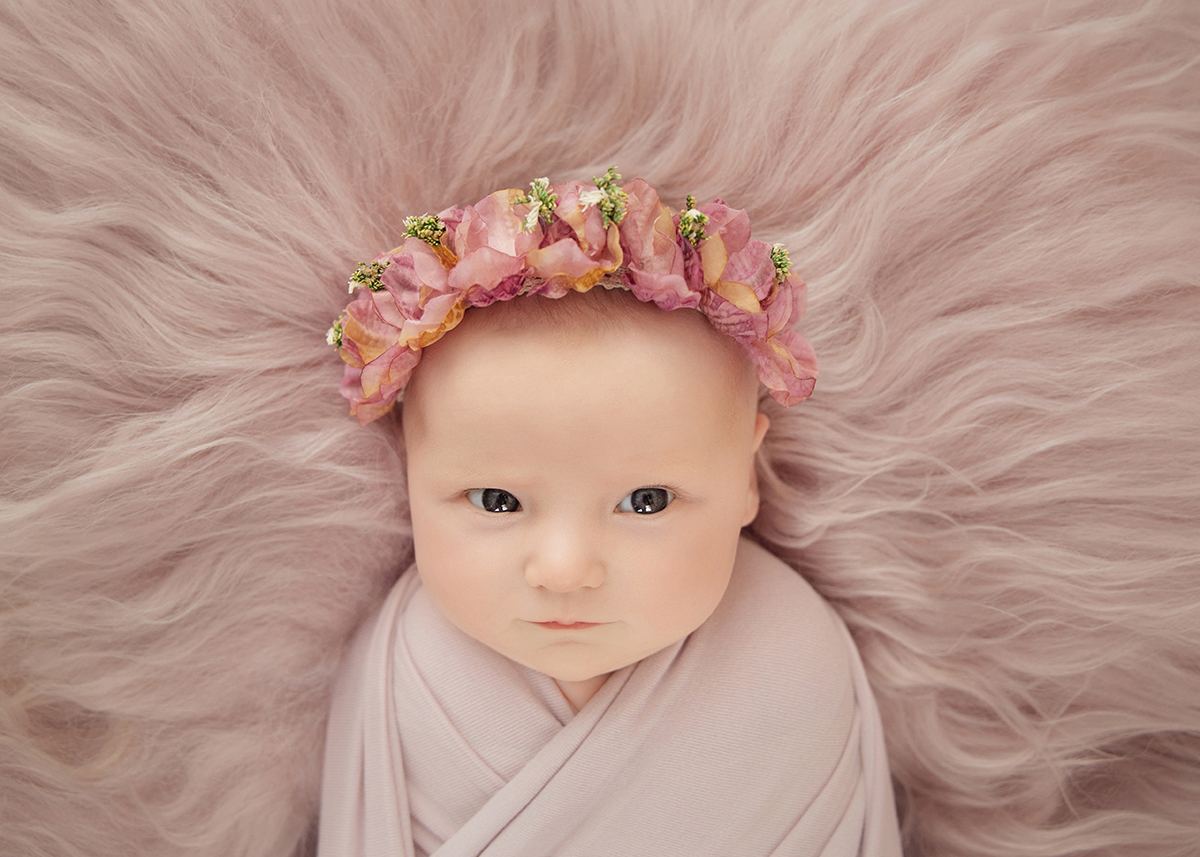 Baby girl portrait with delicate floral headband lying on soft pink fur during a professional newborn photography session in Braintree Essex.