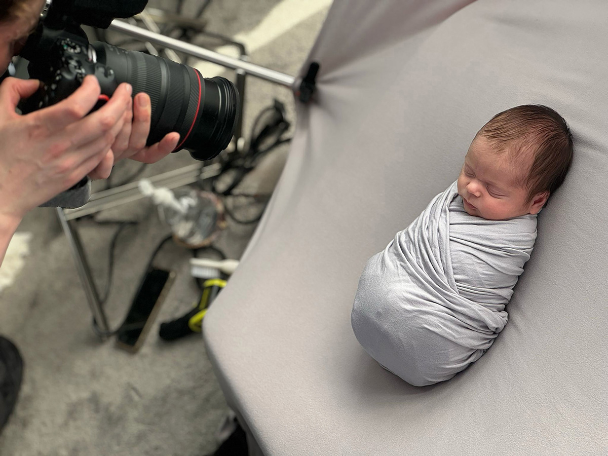 Behind the scenes of a calm in-home newborn photography session in Essex, showing a professional newborn photographer capturing a safely wrapped sleeping baby during a baby-led portrait setup in Chelmsford.
