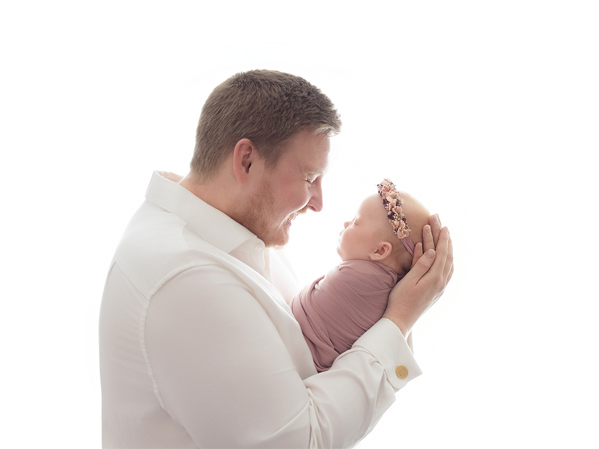 Father lovingly holding his newborn daughter close during a tender newborn photography portrait in Brentwood Essex.