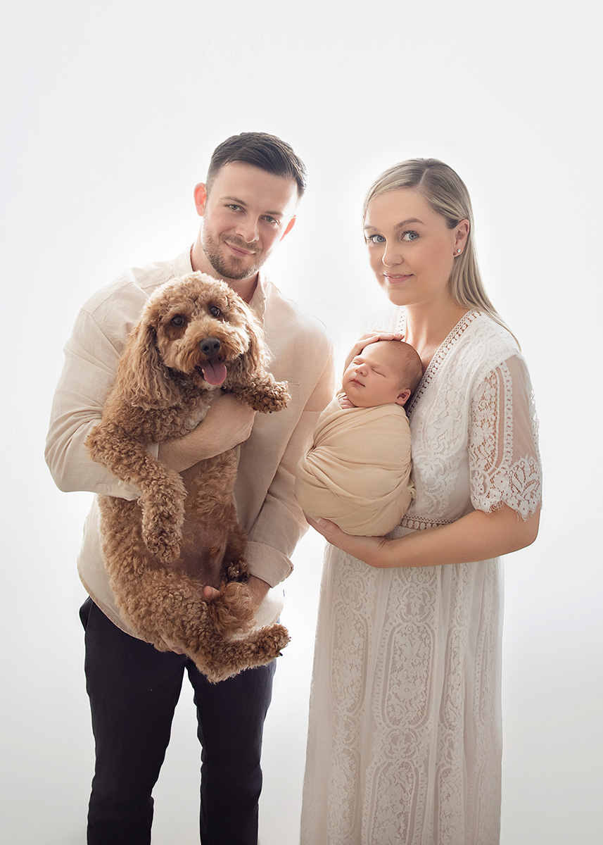 New parents holding their newborn alongside their family dog during a relaxed newborn photography session at home.