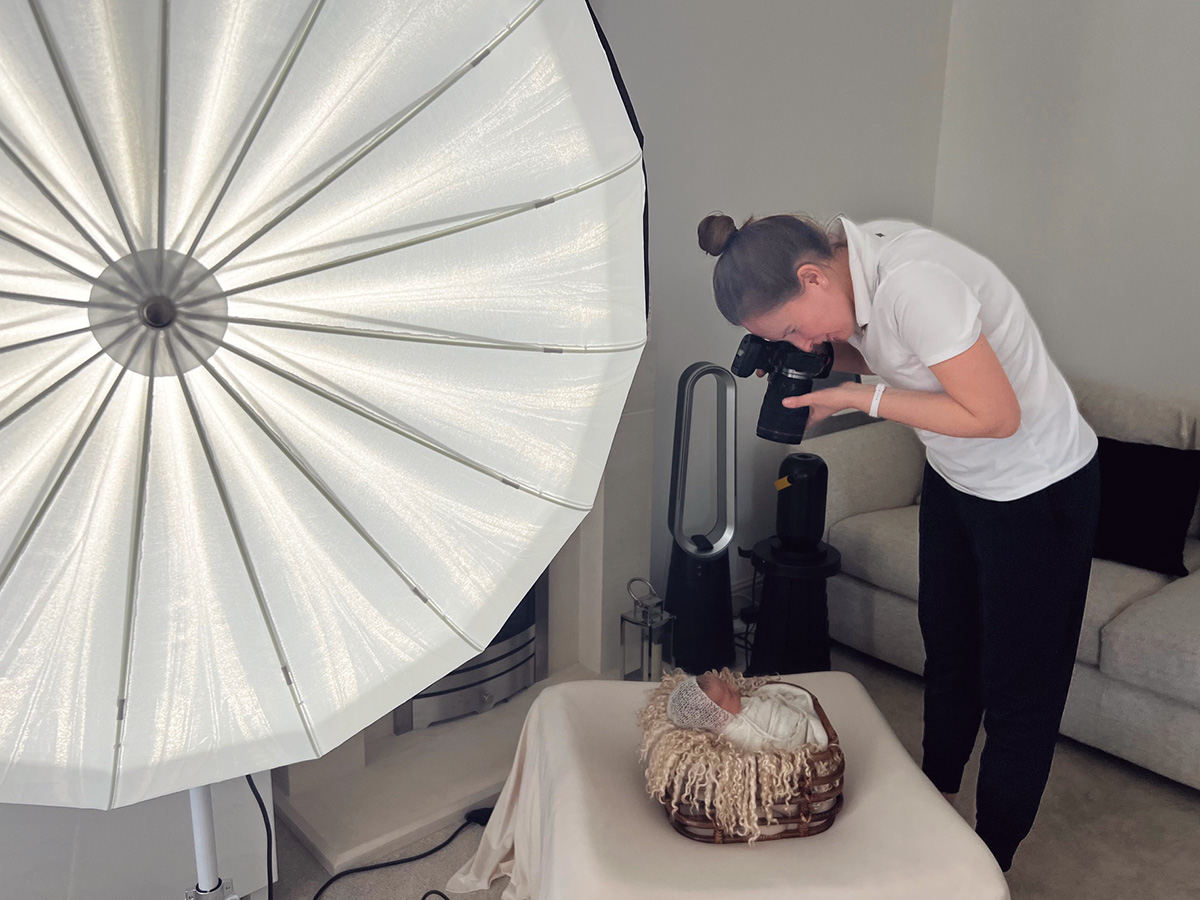 Photographer creating a calm in-home newborn photography session in Essex using professional lighting while baby rests safely in a basket.