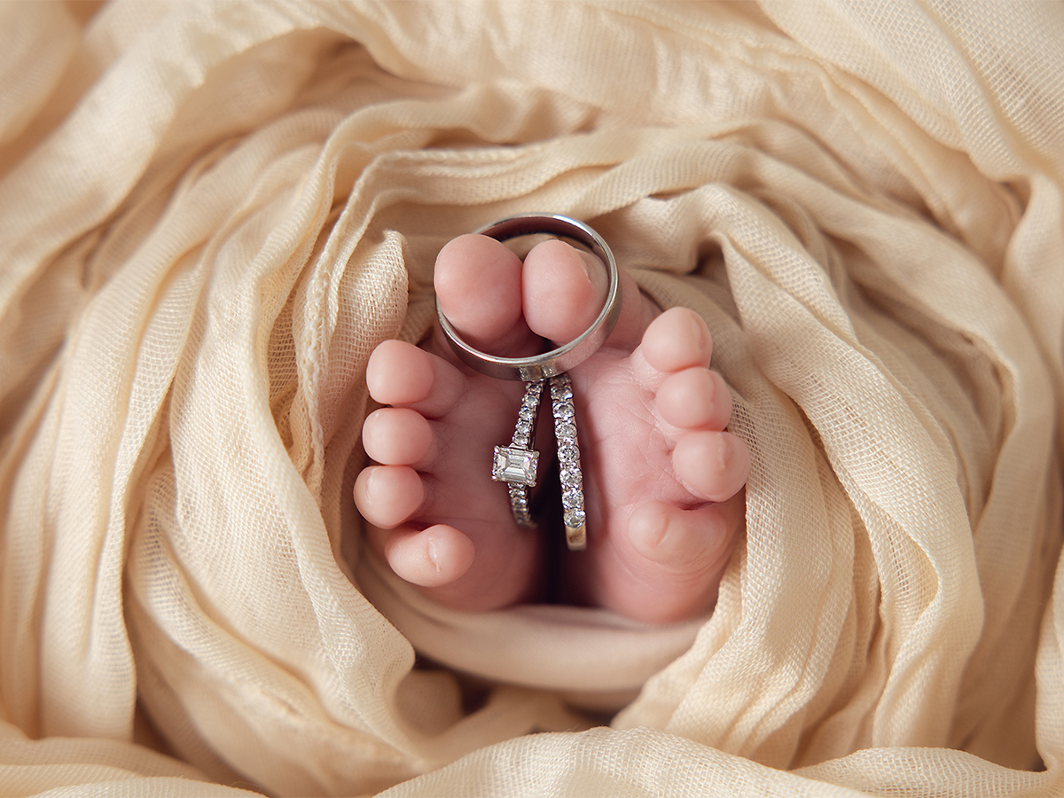 Newborn baby's feet holding parents' wedding and engagement rings during an in-home newborn photography session in Essex.
