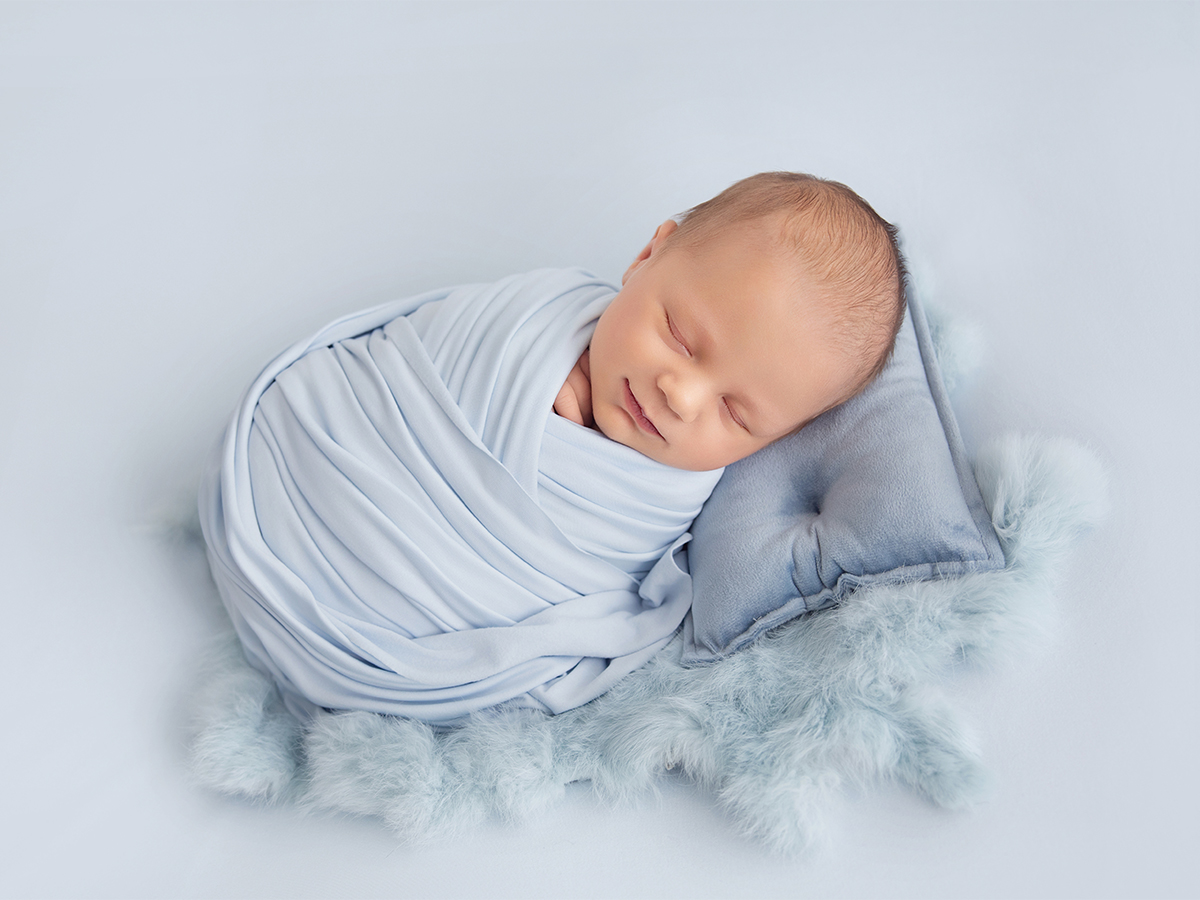 Peacefully sleeping newborn baby boy wrapped in soft blue fabric resting on a fluffy blanket during a newborn photoshoot in Wickford Essex.