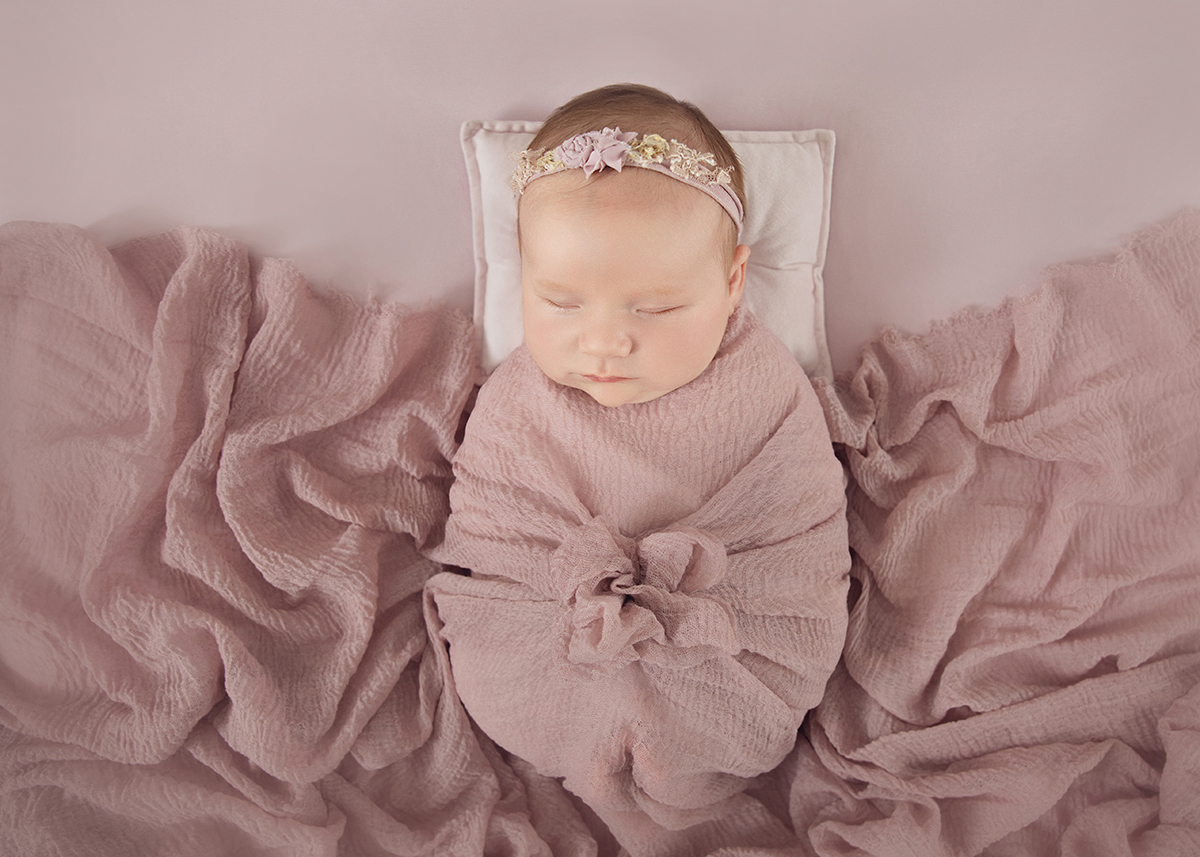 Sleeping newborn baby girl wrapped in soft pink fabric on textured blanket during newborn photography session in Rayleigh Essex.
