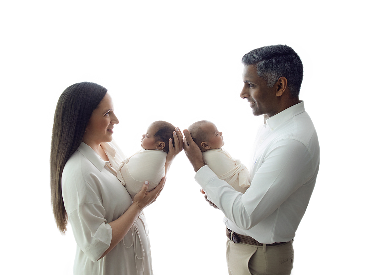 Parents holding their twin newborn babies during an in-home family photography session in Essex, wearing coordinated neutral clothing for timeless newborn portraits.