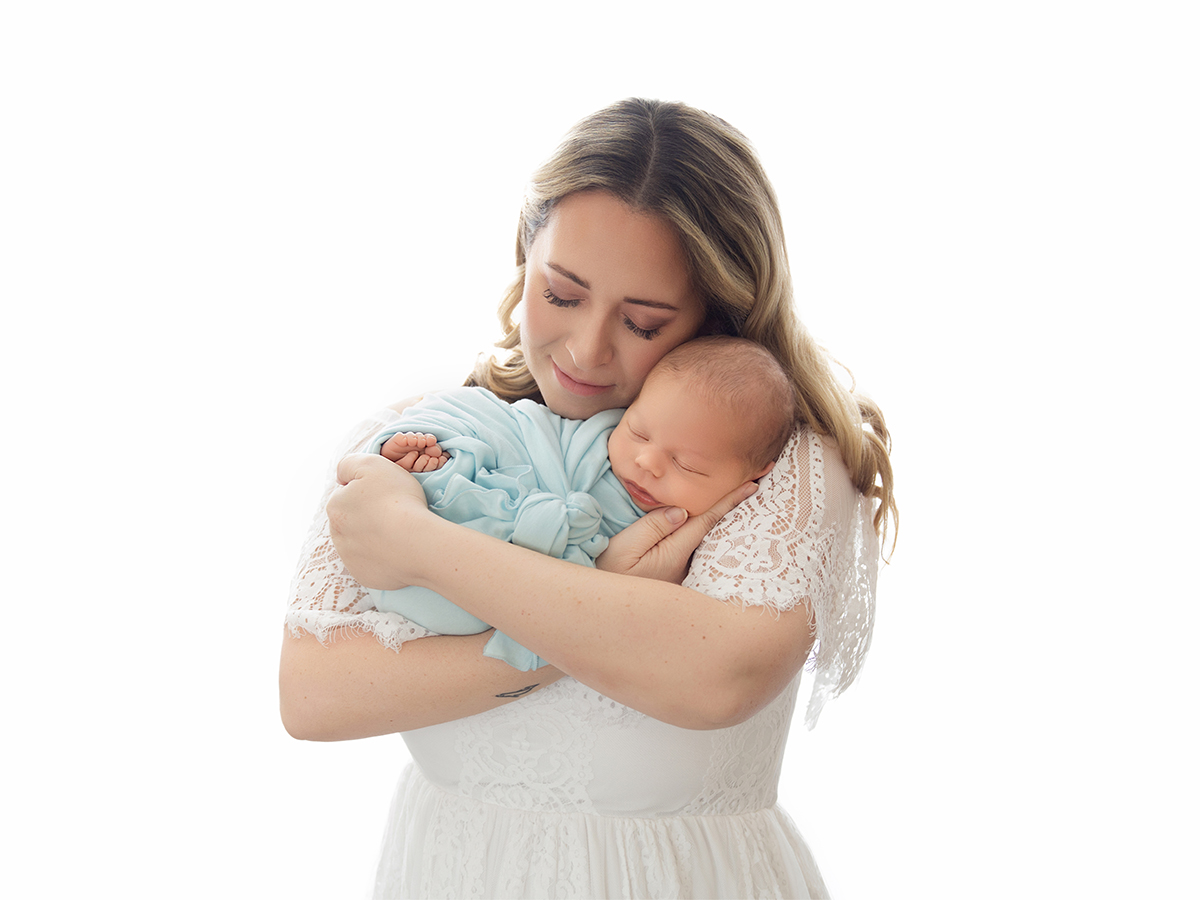 Mother wearing a soft white dress while cuddling her newborn during a relaxed in-home photography session.