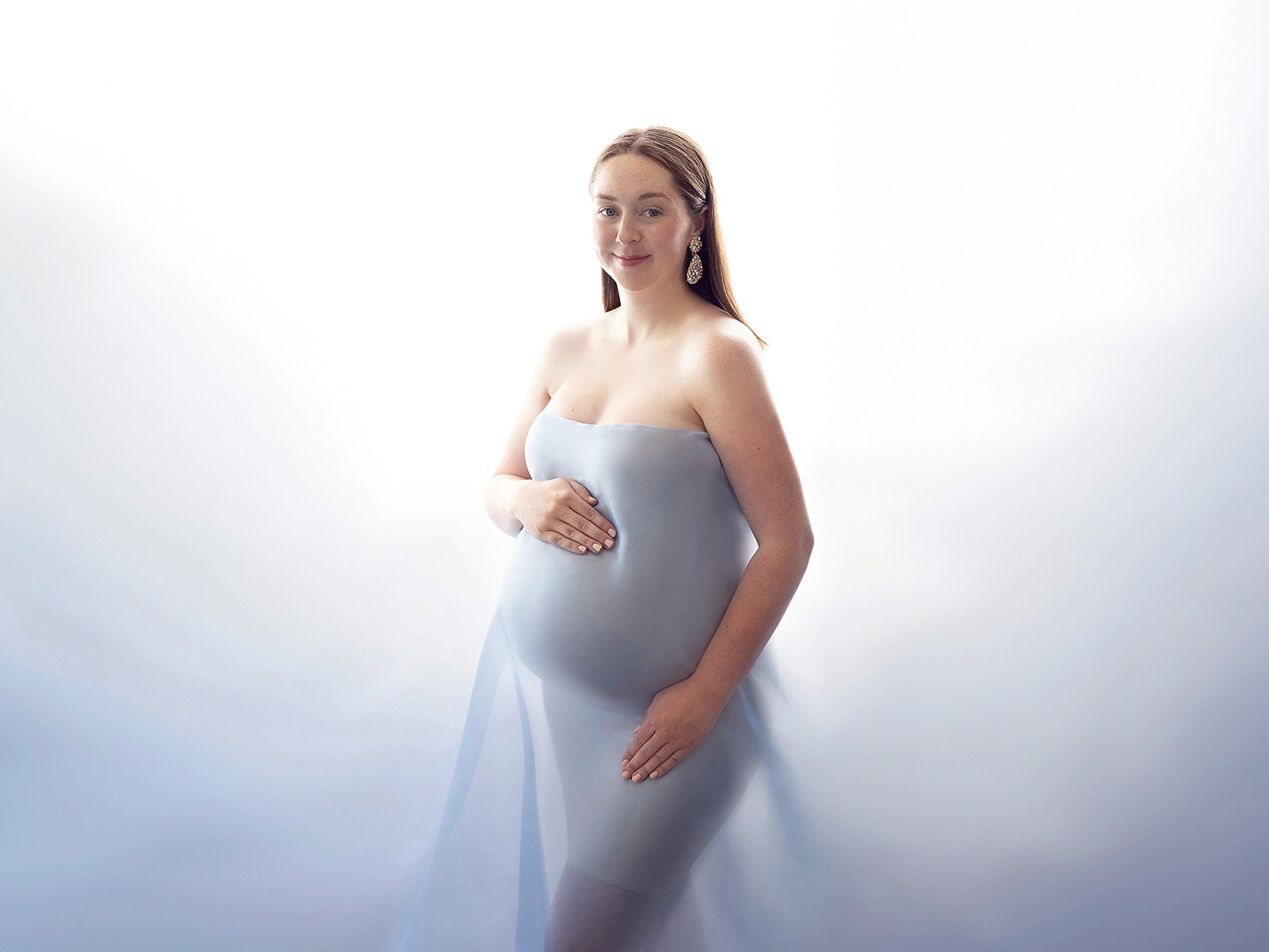Radiant pregnant woman in soft blue fabric, captured in natural light during a professional maternity photoshoot in Essex