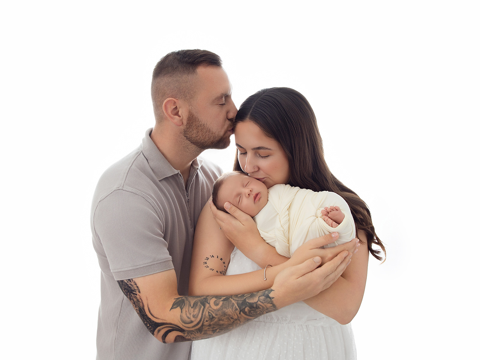 Tender moment of new parents holding and kissing their sleeping newborn baby during an in-home photoshoot in Essex.